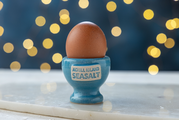 Egg in a blue egg cup labeled 'Achill Island Seasalt' with a festive background