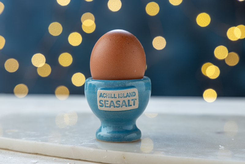 Egg in a blue egg cup labeled 'Achill Island Seasalt' with a festive background