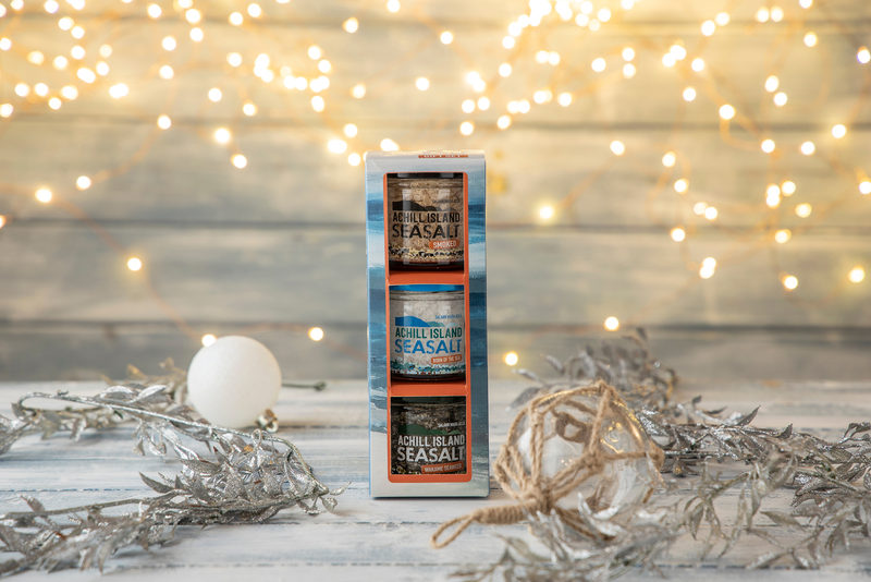 Achill Island Sea Salt Trio gift box on a wooden surface with decorative elements and blurred lights in the background